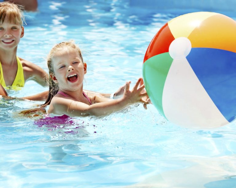 Zwei Kinder im Schwimmbecken spielen mit einem bunten Strandball.