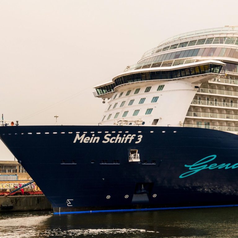 Kreuzfahrtschiff "Mein Schiff 3" im Hafen, mit blauem Schriftzug und moderner Bauweise.