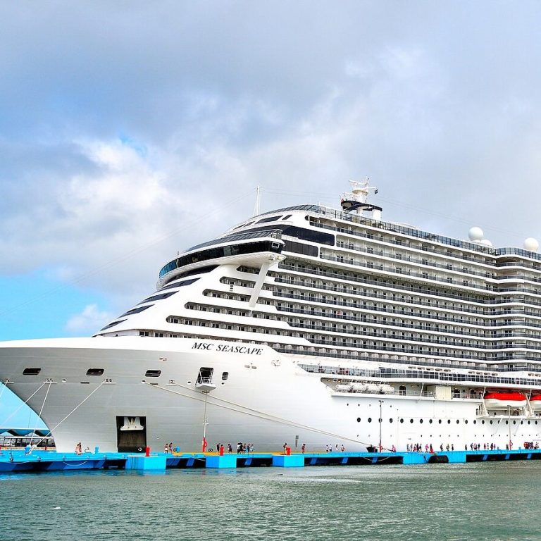 Ein großes Kreuzfahrtschiff im Hafen mit einem blauen Pier. Wolkiger Himmel im Hintergrund.