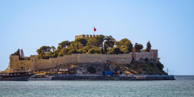 Festung auf einer kleinen Insel, umgeben von Wasser und Bäumen, mit einer Fahne oben.