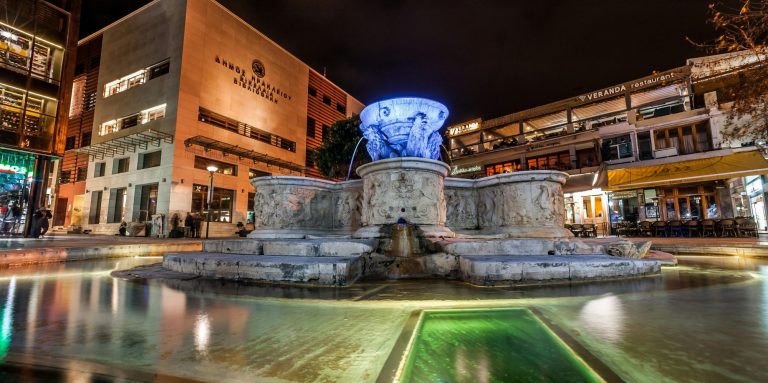 Morosini-Brunnen mit leuchtender Skulptur im belebten Heraklion - Kreta bei Nacht.