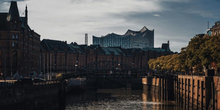 Blick auf historische Gebäude und einen Kanal, mit moderner Architektur im Hintergrund.