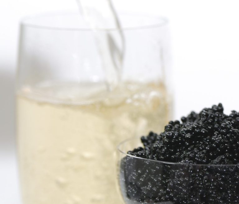 Schwarzes Kaviar in einer Schale neben einem Glas Sekt.