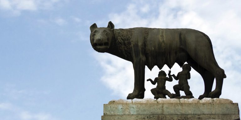 Statue eines Wolfes mit zwei Kindern darunter, gegen einen klaren Himmel.