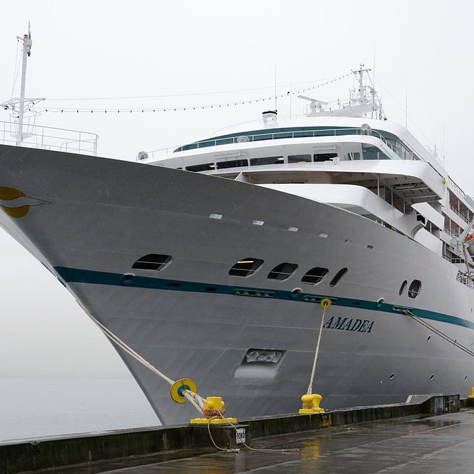 Ein großes Kreuzfahrtschiff am Kai, mit grauem Rumpf und gelben Festmachern.