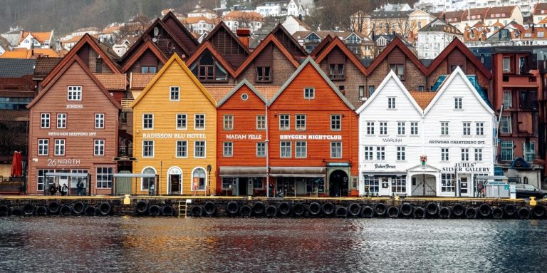 Farbige Häuserfront am Wasser mit Bergen im Hintergrund.