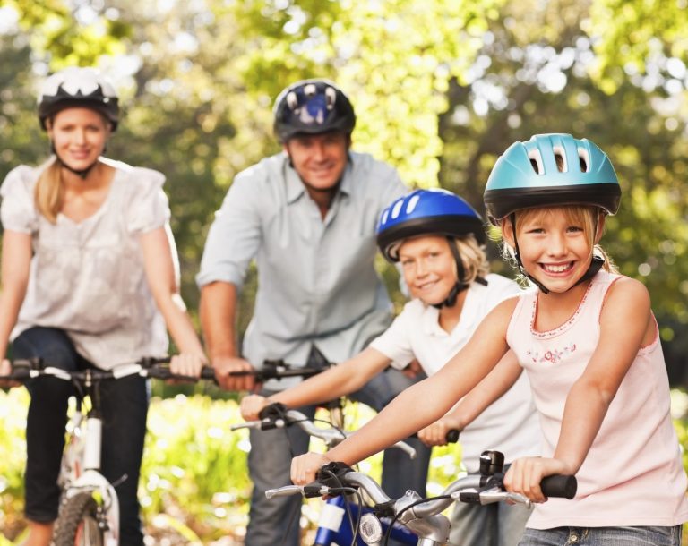 Familie auf Fahrrädern in einem sonnigen Park, fröhliche Gesichter und bunte Helme.